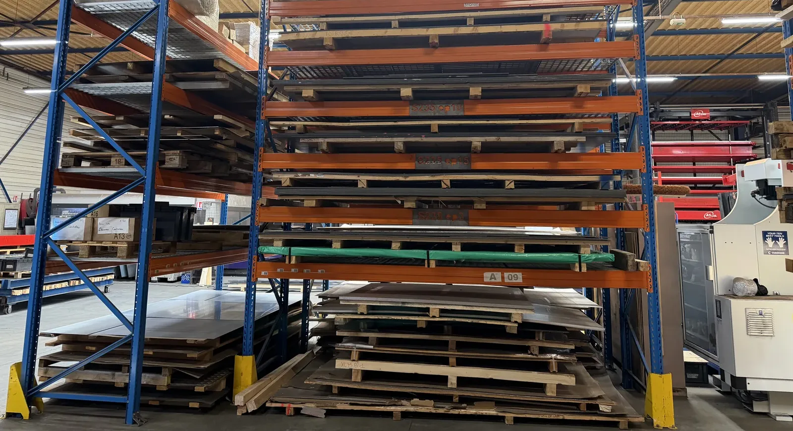 Stock de tôles acier S235, inox et aluminium classées par épaisseur sur racks dans l'atelier AICC