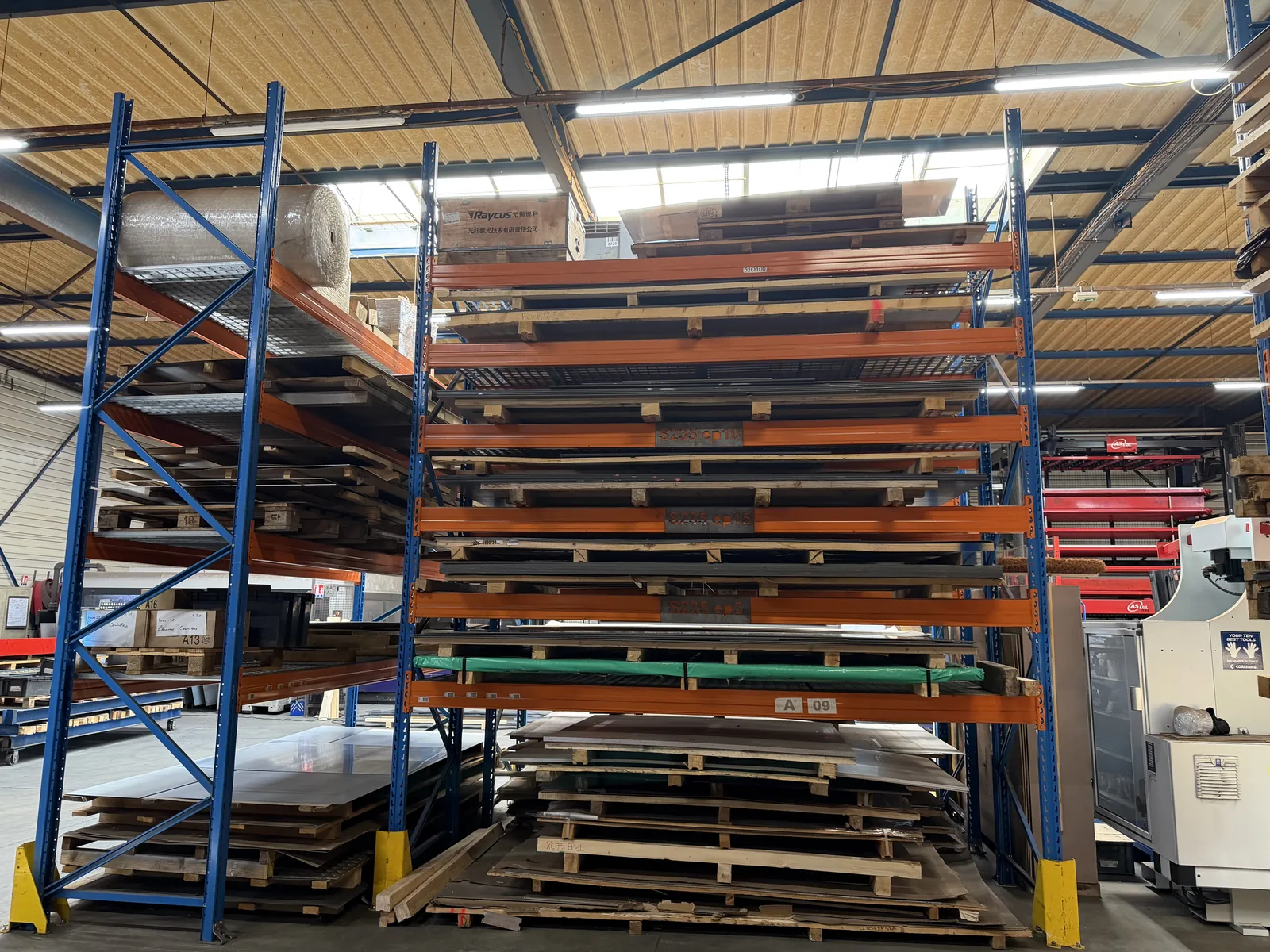 Stock de tôles acier S235, inox et aluminium classées par épaisseur sur racks dans l'atelier AICC