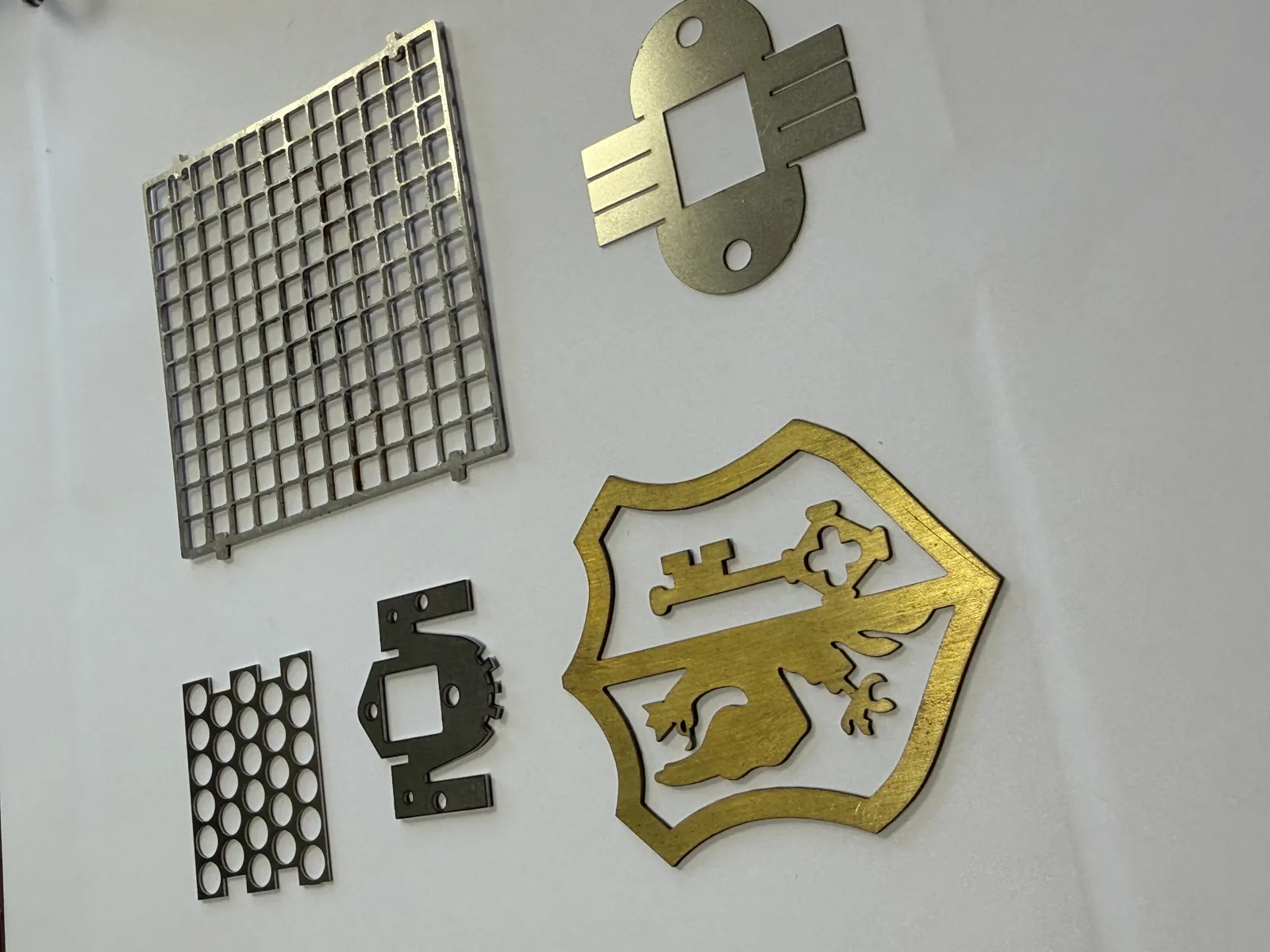 Pièces de découpe laser fine réalisées par AICC : grille ajourée, blindage perforé et écusson en laiton